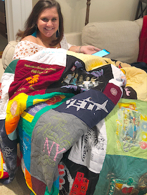 A girl sitting on a couch under her T-shirt quilt by Too Cool T-shirt Quilts